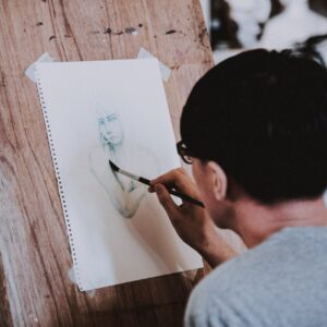 Artist sketching a portrait with a pencil on a wooden easel in a studio setting.