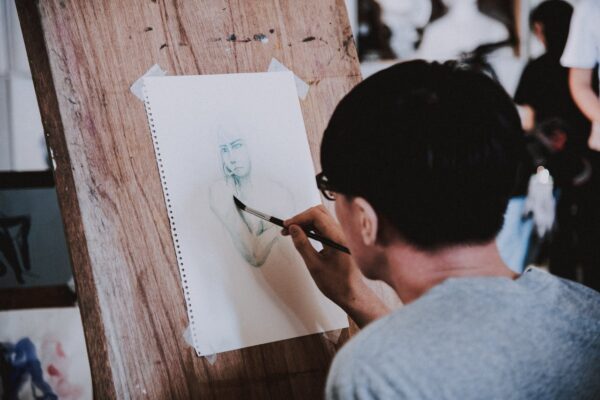 Artist sketching a portrait with a pencil on a wooden easel in a studio setting.