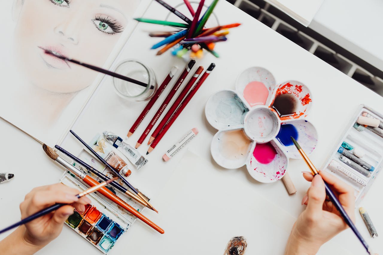 Flat lay of art supplies, including brushes and paint, used in creating a colorful portrait.