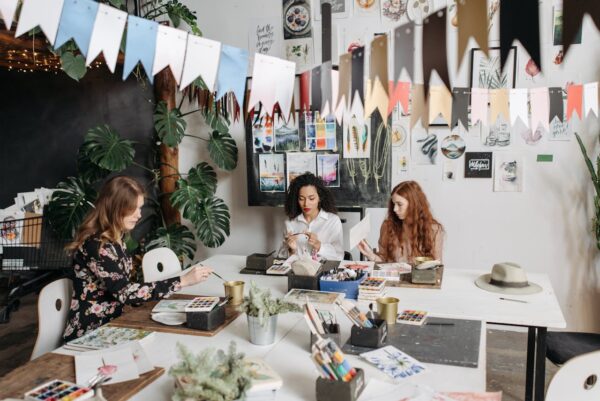 Women engaged in a creative watercolor workshop indoors, surrounded by art supplies and colorful decor.