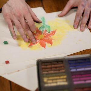 Hands creatively drawing a flower with pastel colors on paper, showcasing hobby art.