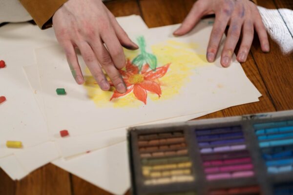 Hands creatively drawing a flower with pastel colors on paper, showcasing hobby art.